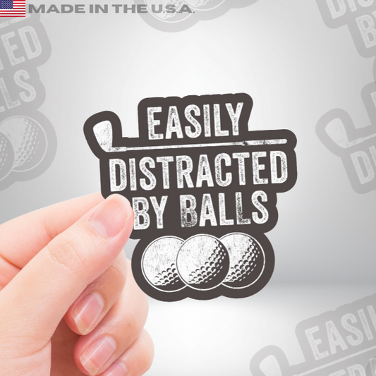 Hand holding a vinyl golf sticker that says "Easily Distracted by Balls" with three illustrated golf balls, humorous gift for golfers.